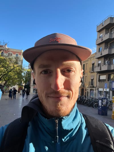 Taylor Jacobson wearing a hat and jacket in a Barcelona plaza, March 2024. 