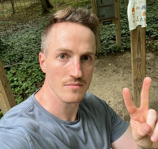 Taylor Jacobson flashing a peace sign on a wooded trail